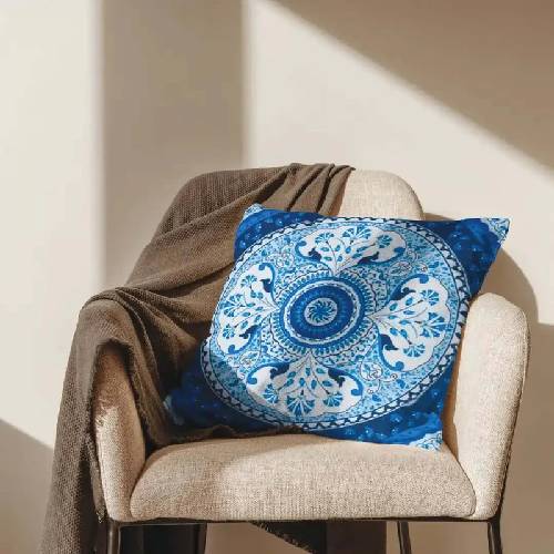 A printed blue mandala cushion by Kolorobia placed on a beige chair with a cozy brown throw, showcasing Kolorobia’s range of artistic home decor and lifestyle products available on their website