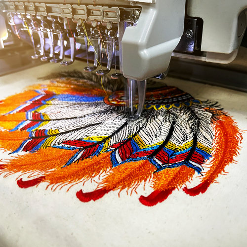 Close-up of an embroidery machine stitching a vibrant feather design on fabric, capturing the embroidery process step in Dhaga-Raga’s personalization journey