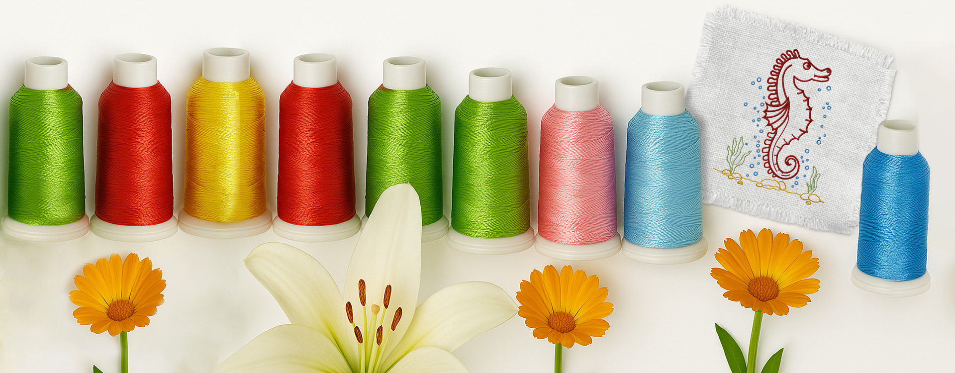 Colorful spools of embroidery thread arranged in a row with vibrant flowers and a white fabric swatch showcasing a red seahorse design