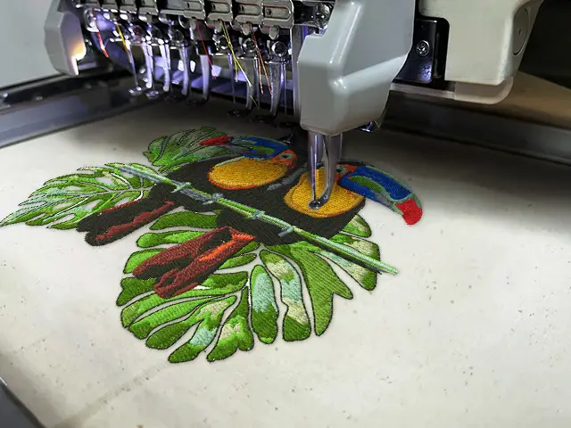 Embroidery machine stitching a colorful toucan bird design on fabric, showcasing the embroidery process at Dhaga Raga