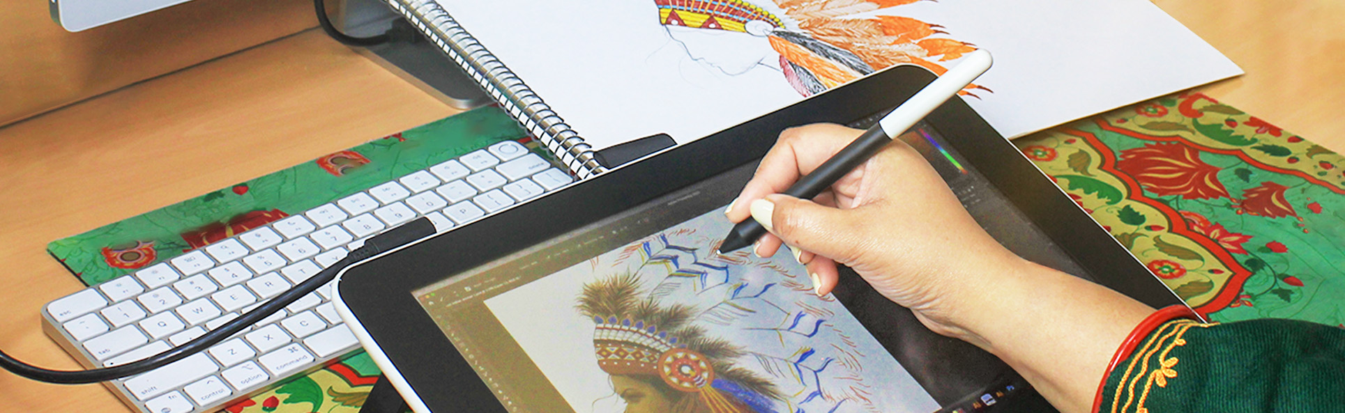 Designer creating a digital embroidery pattern on a tablet, with a hand-drawn sketch and color palette placed on a wooden table