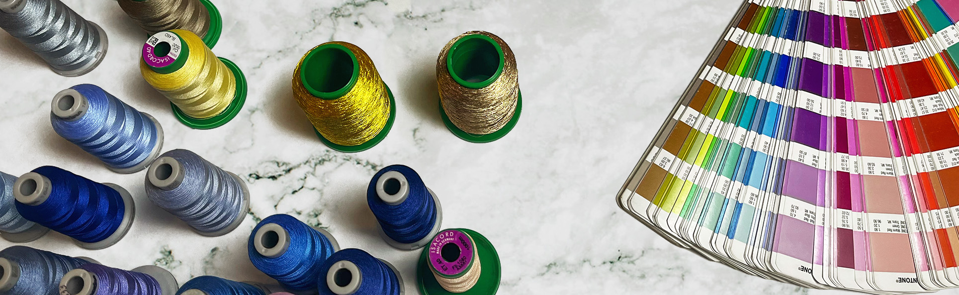 Top view of colorful embroidery threads and Pantone color swatches placed on a marble table for custom embroidery selection