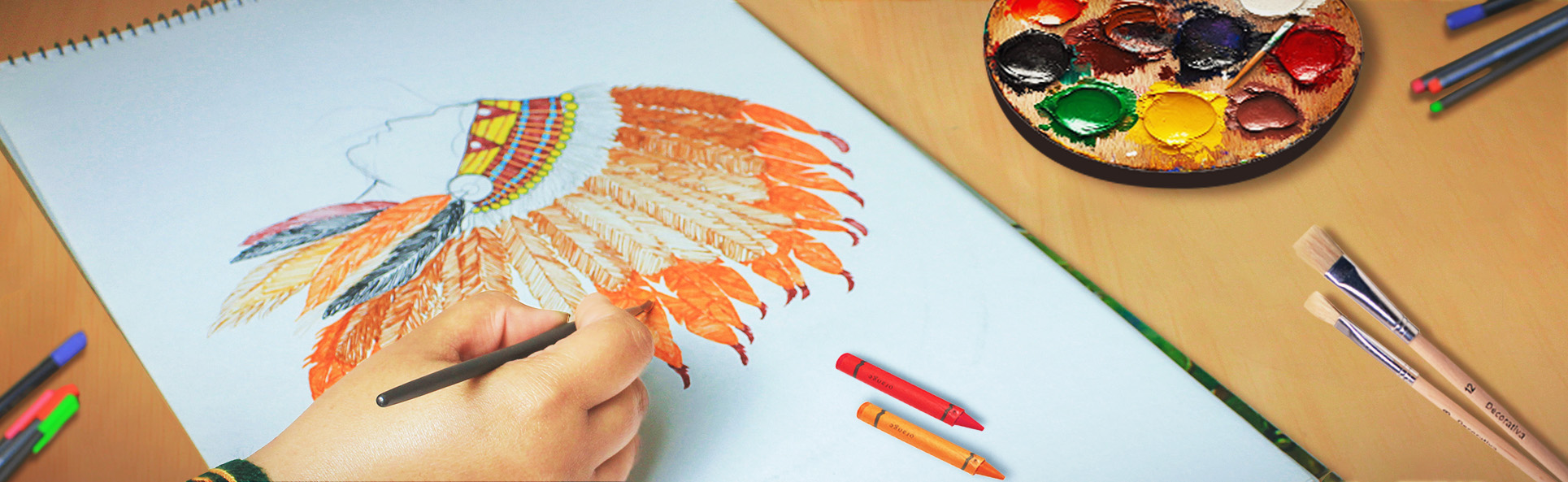 Artistic embroidery design sketching process with hand-coloring feathers using crayons and paint palette on a studio desk