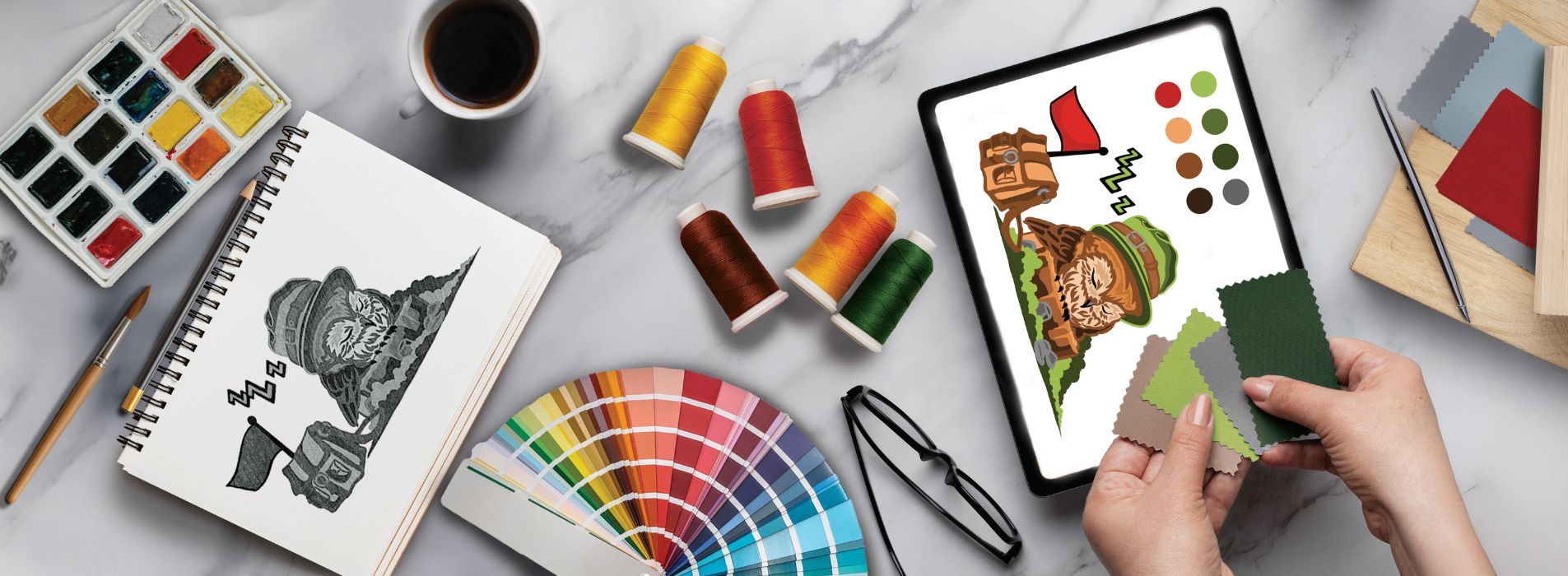 Artist sketching an embroidery design on paper, surrounded by colorful crayons, paints, and design tools, representing the initial creative phase of the personalization process