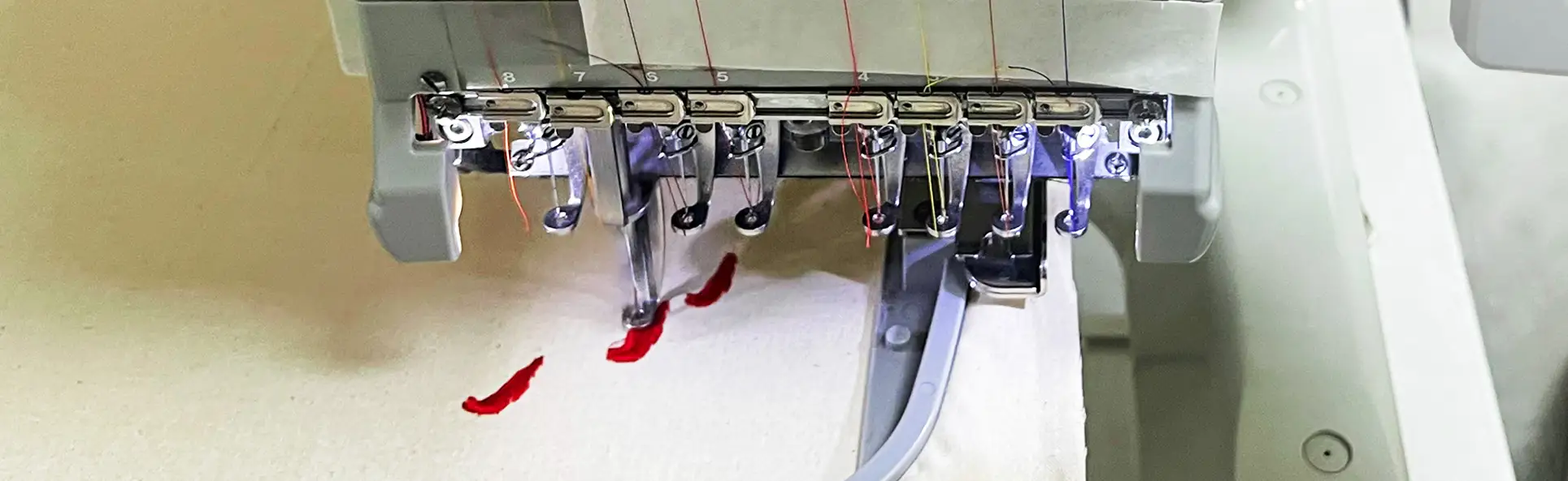 Multi-needle embroidery machine stitching red thread onto fabric, highlighting the precision of custom embroidery work