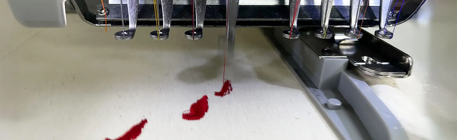 Close-up of an embroidery machine needle stitching red thread onto fabric, capturing the precision of the embroidery process
